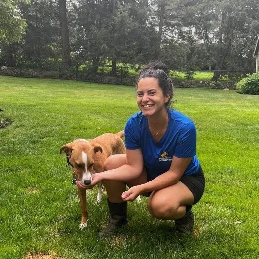 Scooper Ayelen kneeling on a lawn to greet a client's dog