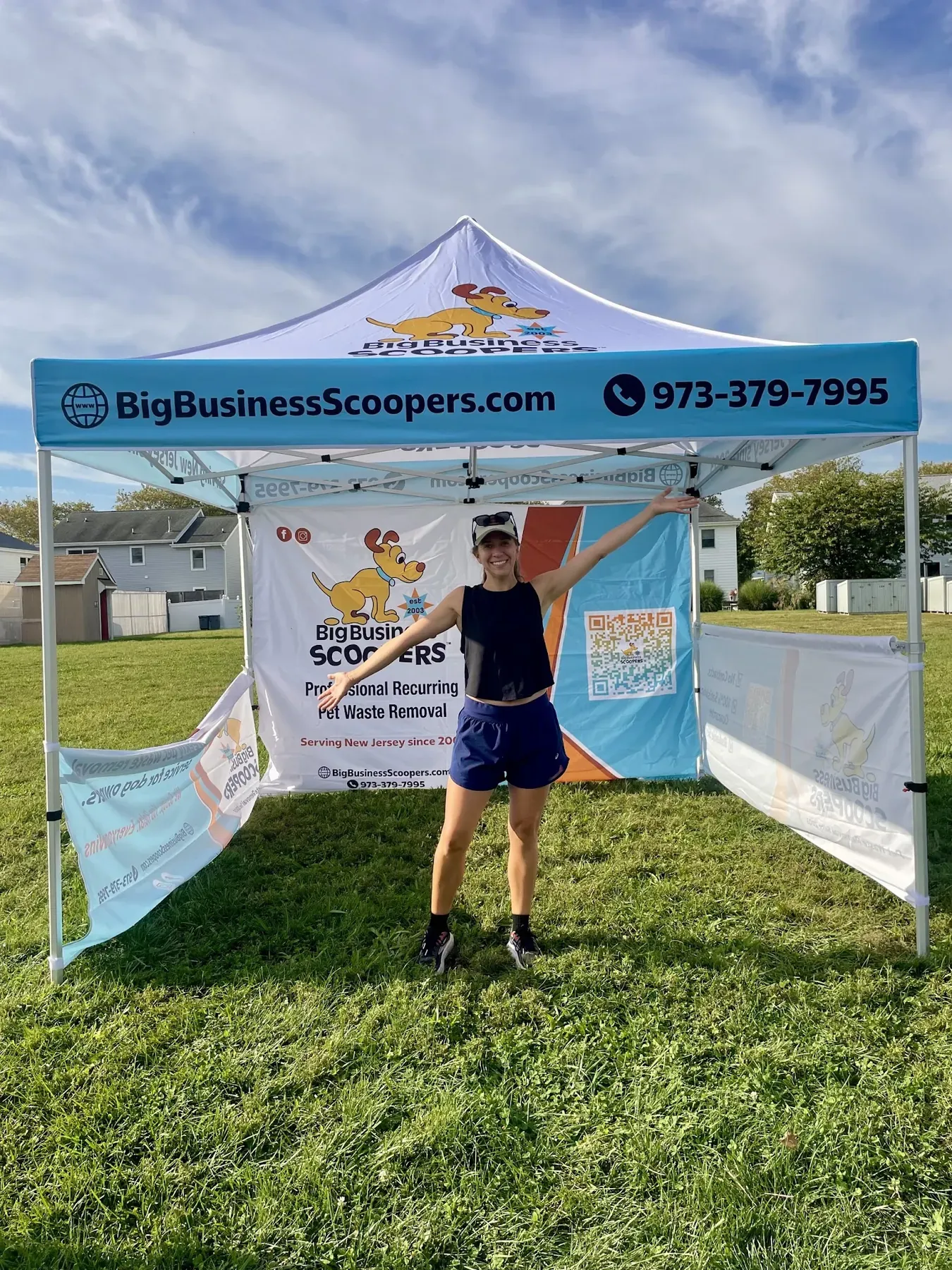 A Big Business Scoopers team member with open arms in front of the company's tent at an outdoor dog event