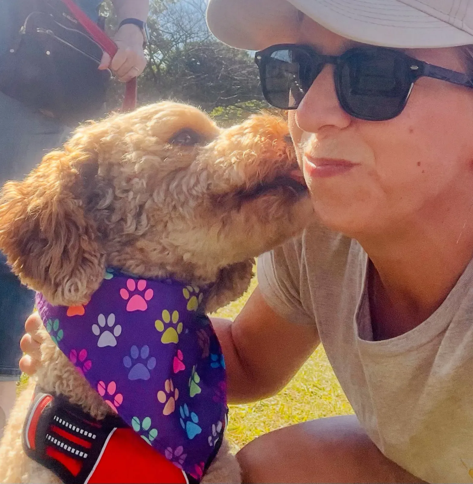 A Big Business Scoopers team member getting a kiss from a curly-coated dog in a paw-print bandana