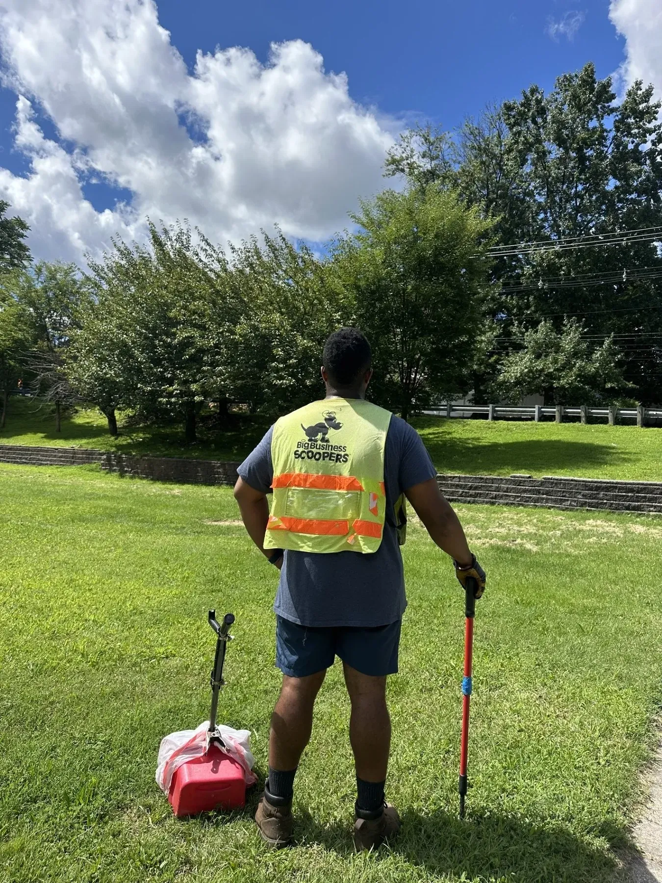 A Big Business Scoopers scooper in a safety vest standing in a yard with a rake and pan