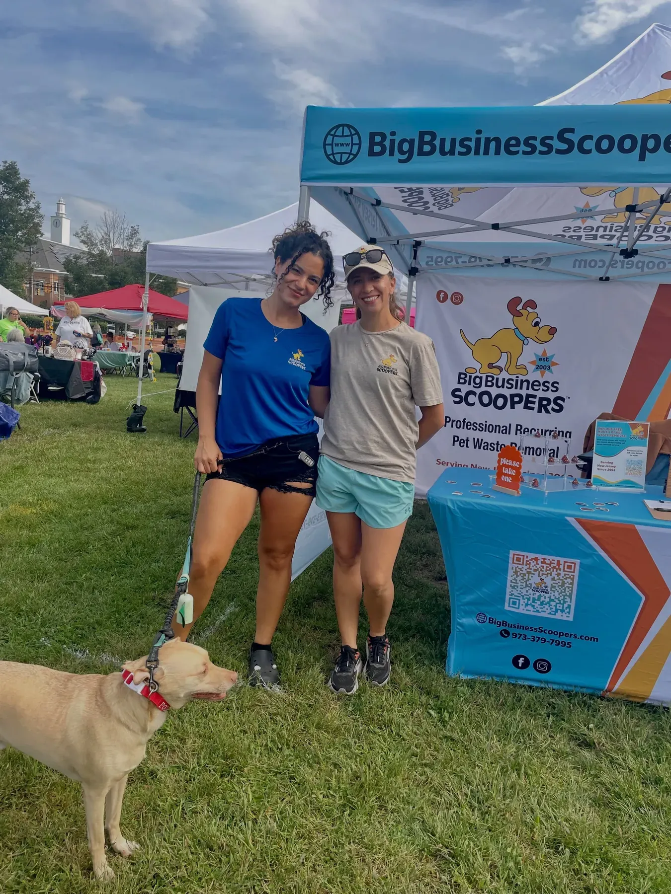 Two Big Business Scoopers team members and a dog at the company's branded tent at a community event